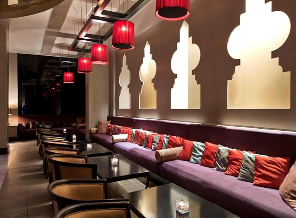 Mūsdienīgs bārs ar siltu apgaismojumu, eksotiskām sienu dekorācijām un komfortablu sēdvietu zonu. Sarkanās lampiņas piešķir telpai intīmu atmosfēru.