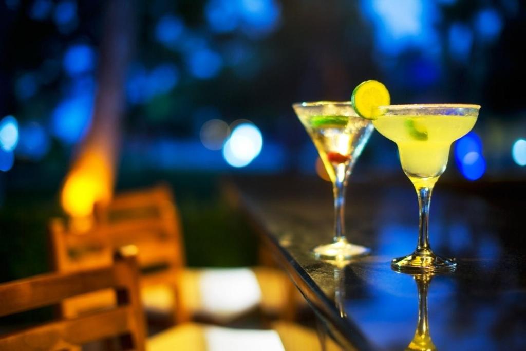 Divi kokteiļi ar citrona un laima šķēlītēm, izvietoti uz galda, ar izplūdušu fona apgaismojumu. Ideāli piemēroti vakara relaksācijai.