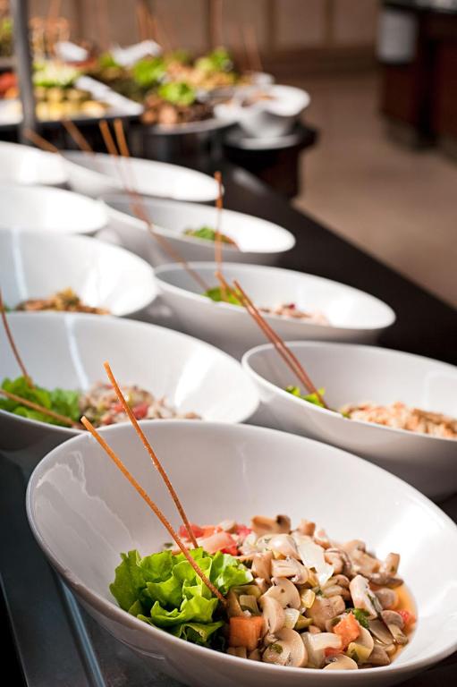 Svaigu salātu bļodas ar dārzeņiem un garšaugiem, izkārtotas uz melna galda, piedāvā krāsainu un veselīgu ēdienu izvēli.