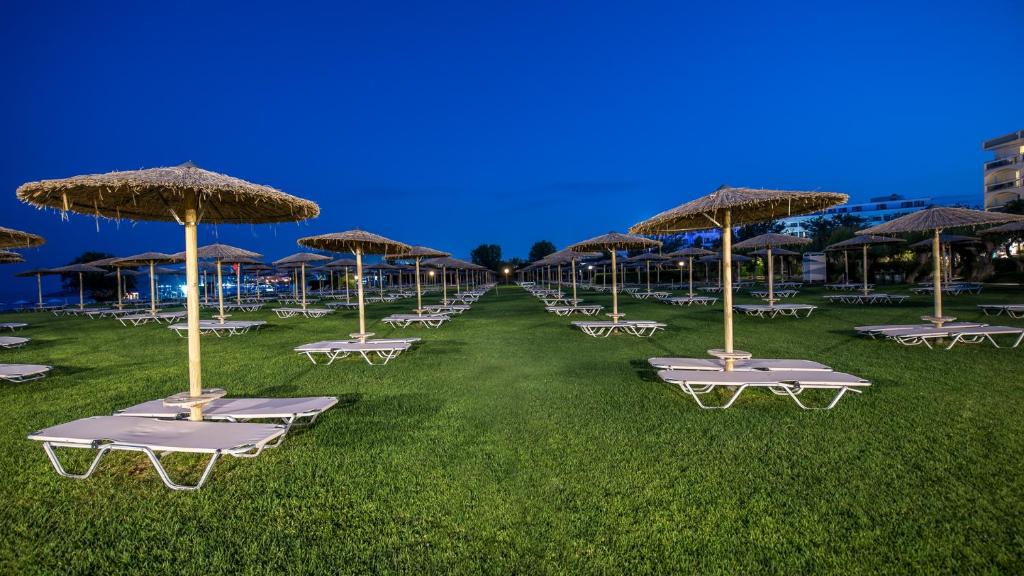 Pludmales ainava ar saulessargiem un guļamkrēsliem, kas izvietoti uz zaļās zāles nakts laikā. Ideāla vieta atpūtai un relaksācijai.