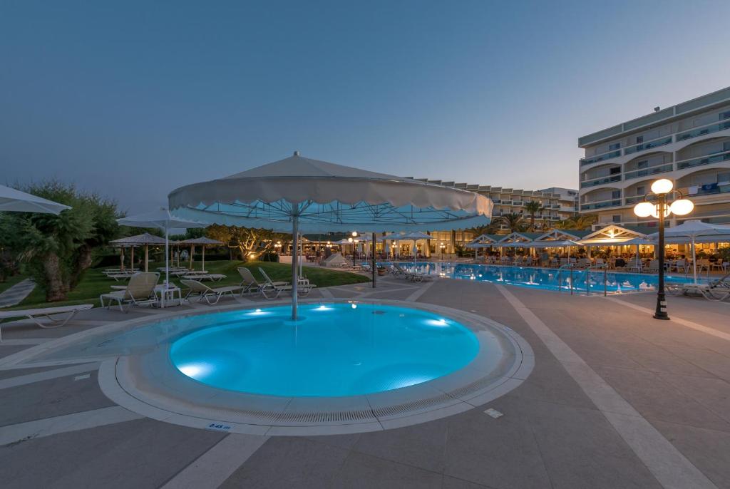 Baseins ar gaismas efektu, ēnainie lietussargi un viesnīcas komplekss fonā, kas rada relaksējošu atmosfēru. Ideāla vieta atpūtai un atvaļinājumam.