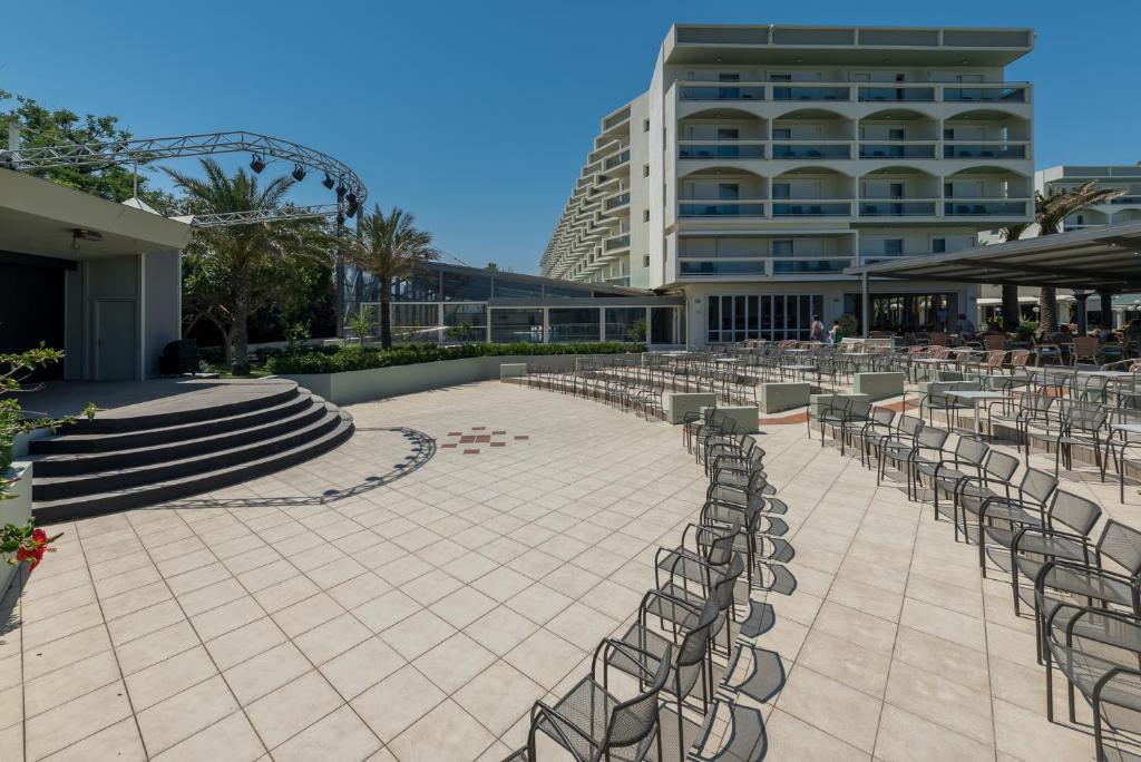 Moderns viesnīcas pagalms ar soliem un skatuvi, ko ieskauj palmas, un saule spīd debesīs. Ideāla vieta pasākumiem un atpūtai.