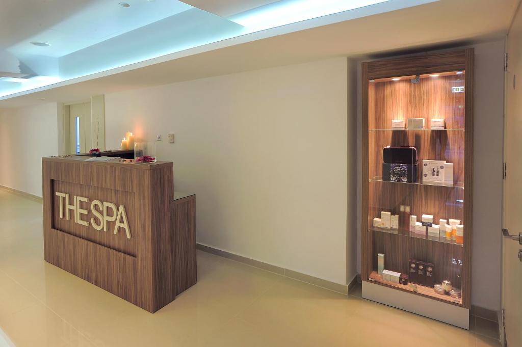 Moderns spa reģistratūras interjers ar koka akcentiem un produktiem izstādē. Telpa ir gaiša un eleganta, radot relaksējošu atmosfēru.