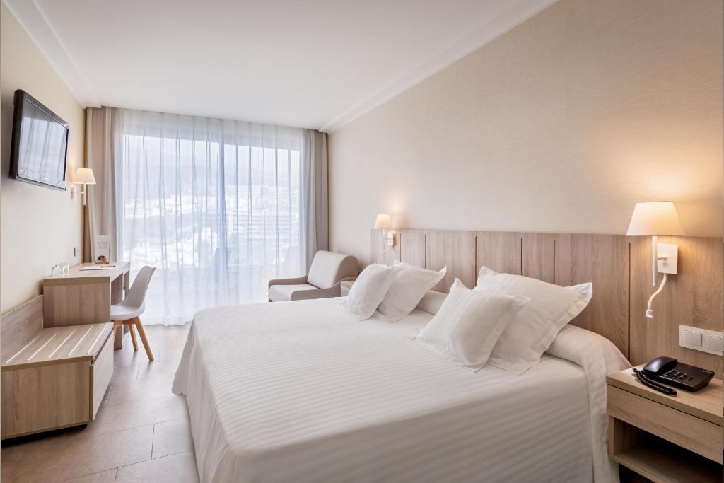 Mūsdienīgs viesnīcas numurs ar divguļamo gultu, rakstāmgaldu un viesistabu, caur kuru ieplūst dabiska gaisma. Logu priekšā ir caurspīdīgas aizkari, radot gaišu un ērtu atmosfēru.