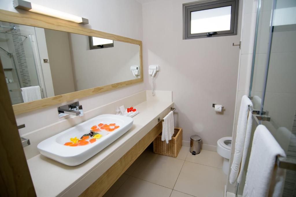 Moderns vannas istabas dizains ar gaišām krāsām un elegantu izskatu. Izceļas baltā izlietne ar ziedlapiņām un liela spoguļa klātbūtne.