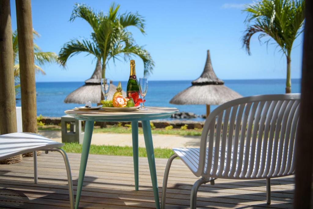 Romantiska brīvdienu ainava ar galdu, uz kura ir šampanietis un augļi, un skats uz okeānu, kurā redzamas palmām un salmu jumtiem. Ideāla vieta relaksācijai un svinībām.