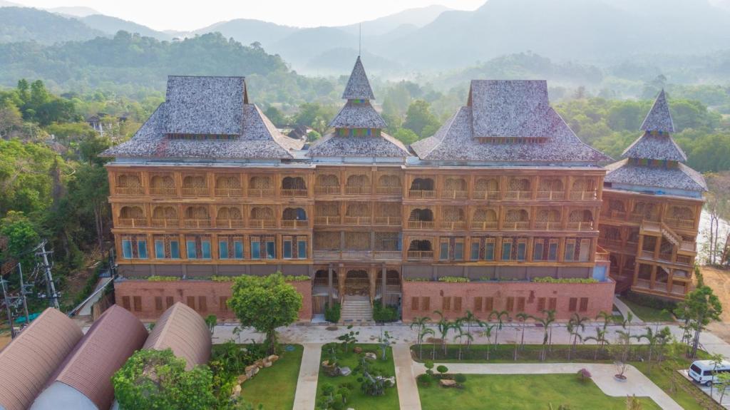 Vides skats uz elegantu koka ēku ar tradicionālu arhitektūru, ko ieskauj kalni un dabiska ainava. Apkārtne ir zaļa un labi kopta, radot mierīgu atmosfēru.