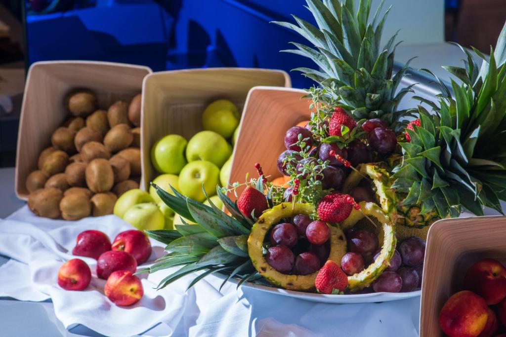 Augļu kompozīcija ar ananāsiem, vīnogām, zemenēm, kivi un āboliem, pasniegta uz balta galdauta.