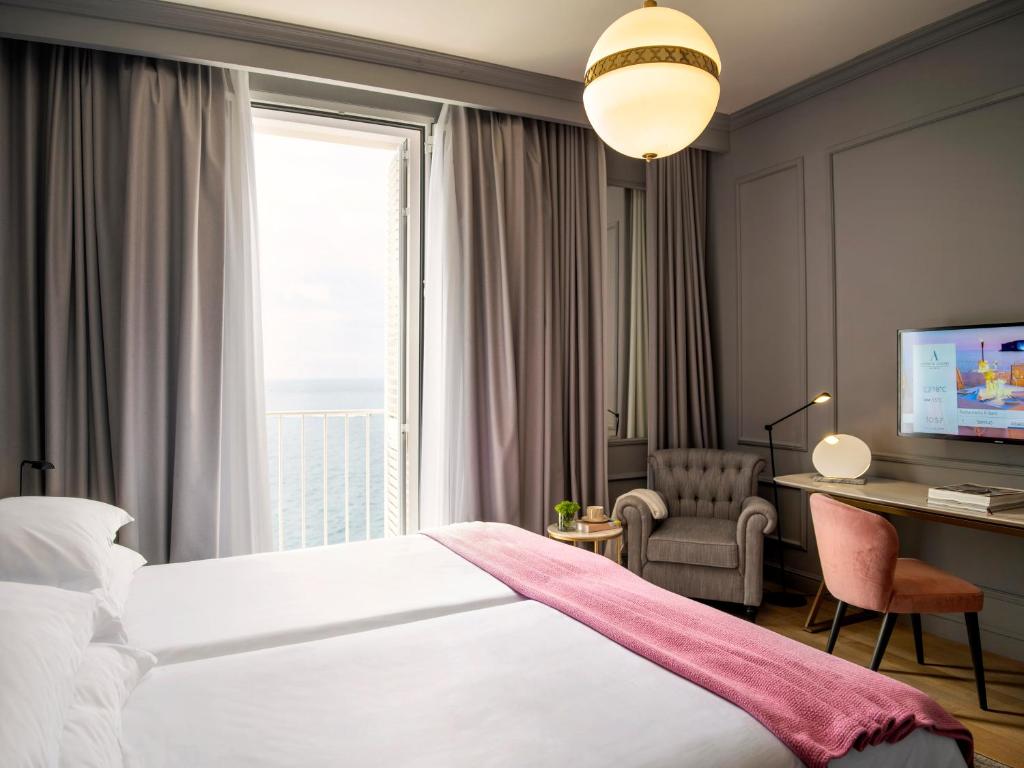 Mūsdienīgs viesnīcas numurs ar skatu uz jūru, iekārtots ar divām gultām, ērtu krēslu un televizoru. Interjers ir gaišs un elegants, ar mīkstām aizkaru drānām un siltām krāsām.