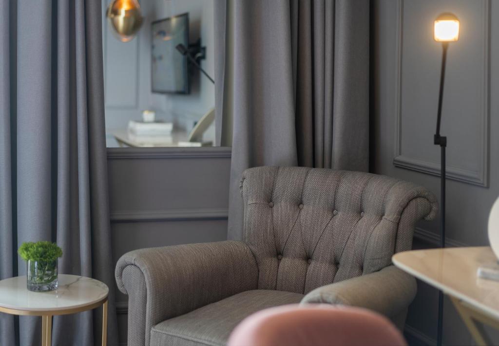 Mūsdienīgs dzīvojamās istabas interjers ar pelēku dīvānu, blakus nelielai galdiņai un augiem. Gaišas aizkari un siltā apgaismojuma lampa rada patīkamu atmosfēru.