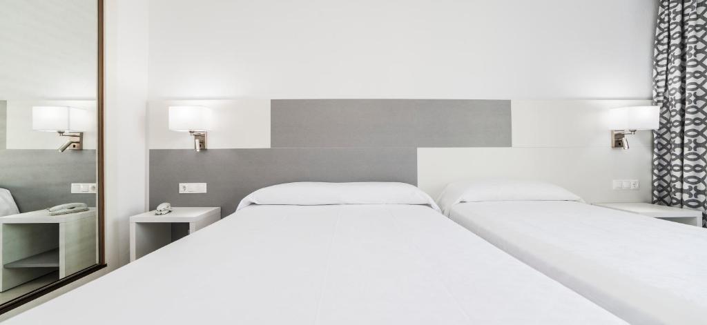 Mūsdienīgs viesnīcas numurs ar divām gultām, gaišām sienām un dekoratīvām aizkaru. Numurā redzama spoguļa siena un naktsgaldiņš.