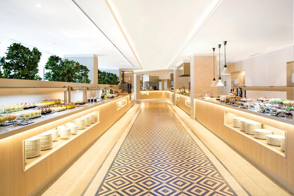 Mūsdienīga bufete ar plašu ēdienu izvēli un elegantu interjeru, kas iekļauj zaļos augus un stilīgu grīdas dizainu.