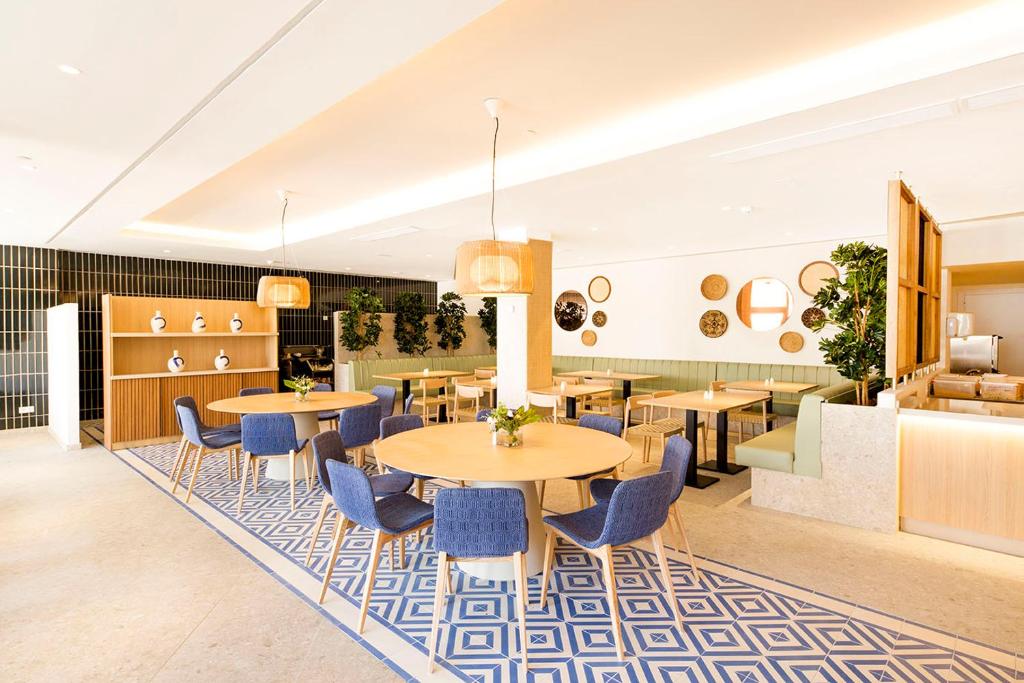 Mūsdienīgs restorāns ar gaišu interjeru, koka mēbelēm un elegantu grīdas segumu, kas rada patīkamu atmosfēru. Svaigi zaļumi un dekoratīvi elementi papildina dizainu.