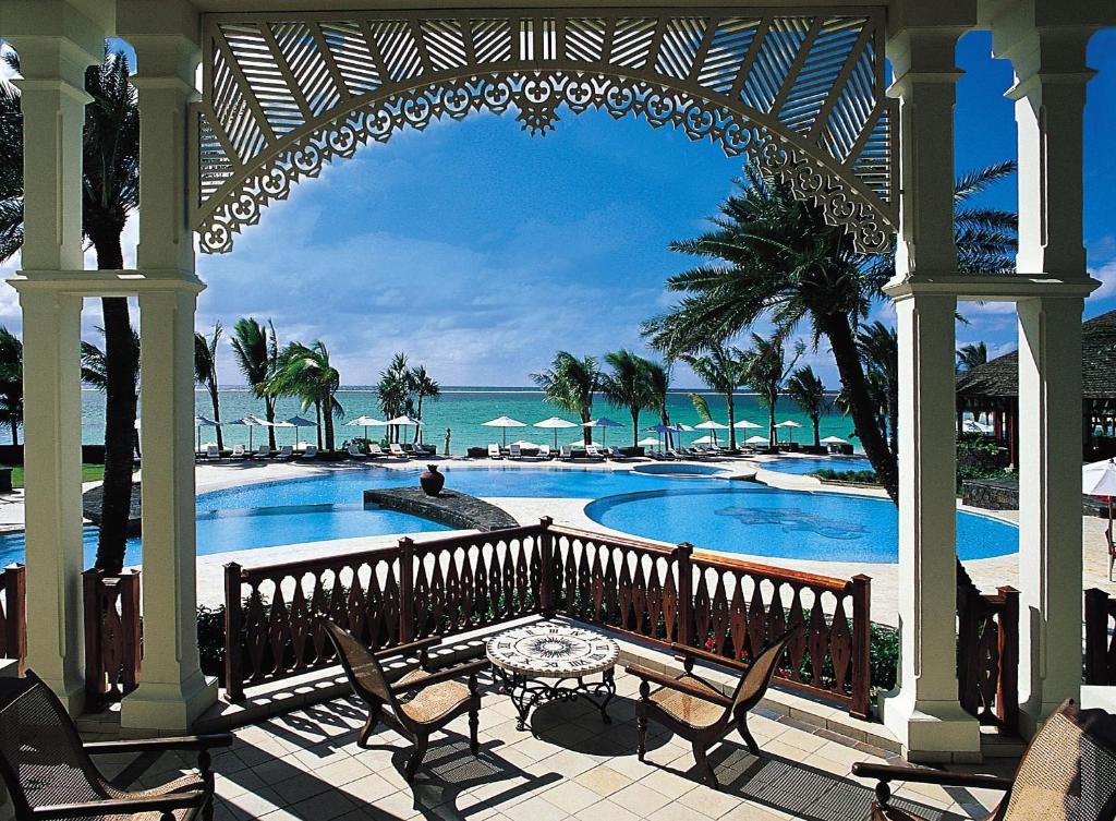 Tropu kūrorts ar pludmali un baseinu, skats no verandas. Zilais debesis un palmas rada mierīgu atmosfēru.