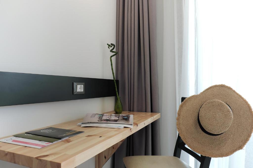 Mūsdienīga interjera stūra ar koka galdu, krēslu un dekoratīvu augu. Uz galda atrodas žurnāli un cepure, kas rada mājīgu atmosfēru.