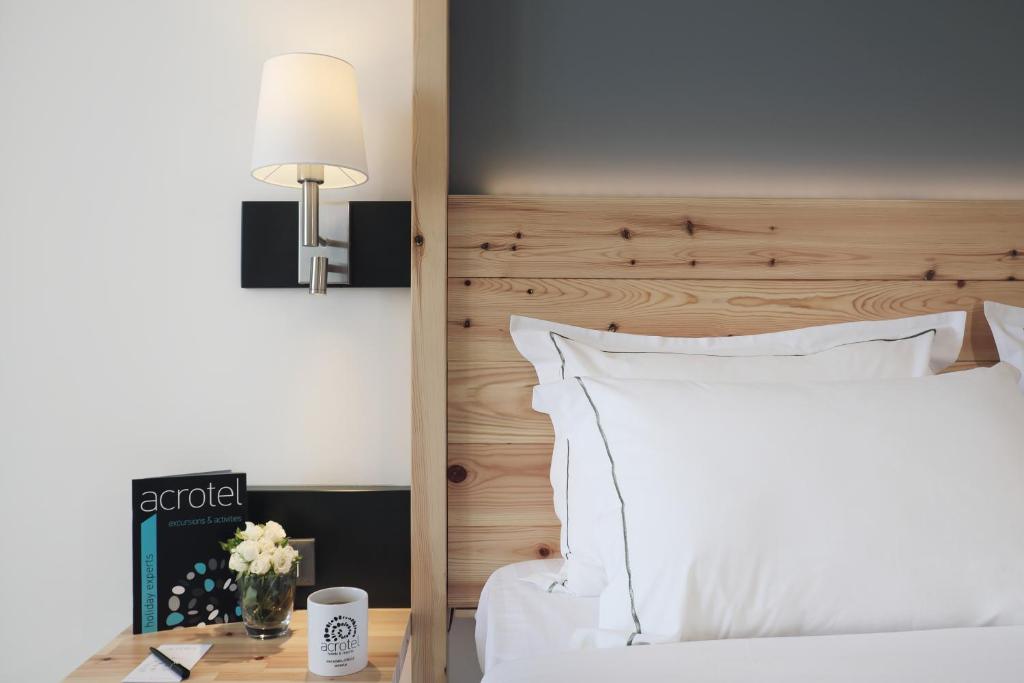 Mūsdienīgs guļamistabas interjers ar koka gultas galvu, baltām gultas veļām un naktslampu, blakus ziedu kompozīcija un žurnāls uz galda.