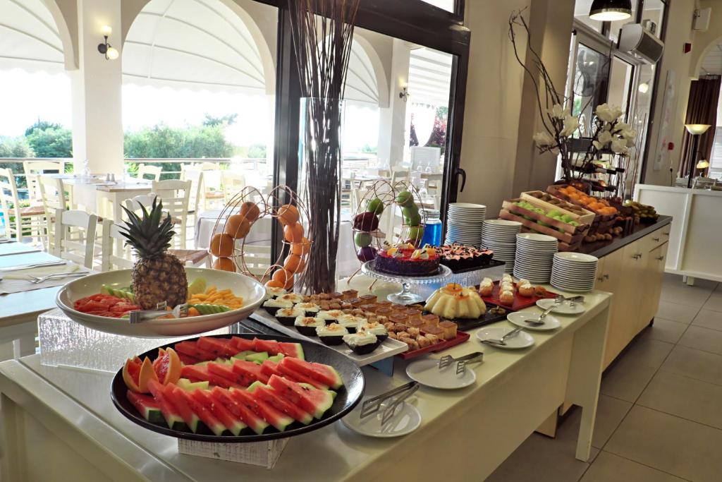 Bagātīgs bufetes galds ar dažādiem augļiem, desertiem un uzkodām, apgaismots ar dabiskiem gaismas avotiem un zaļo ainavu ārpusē. Ideāls rīts vai pusdienlaiks ar gardiem ēdieniem.