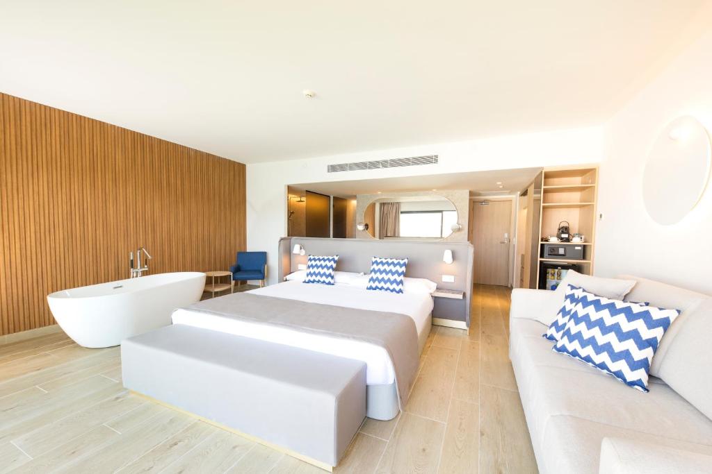 Mūsdienīga viesnīcas numura iekārtojums ar pelēko gultu, dīvānu un vannu. Numurā ir arī koka akcenti un eleganta apgaismojuma dizains.