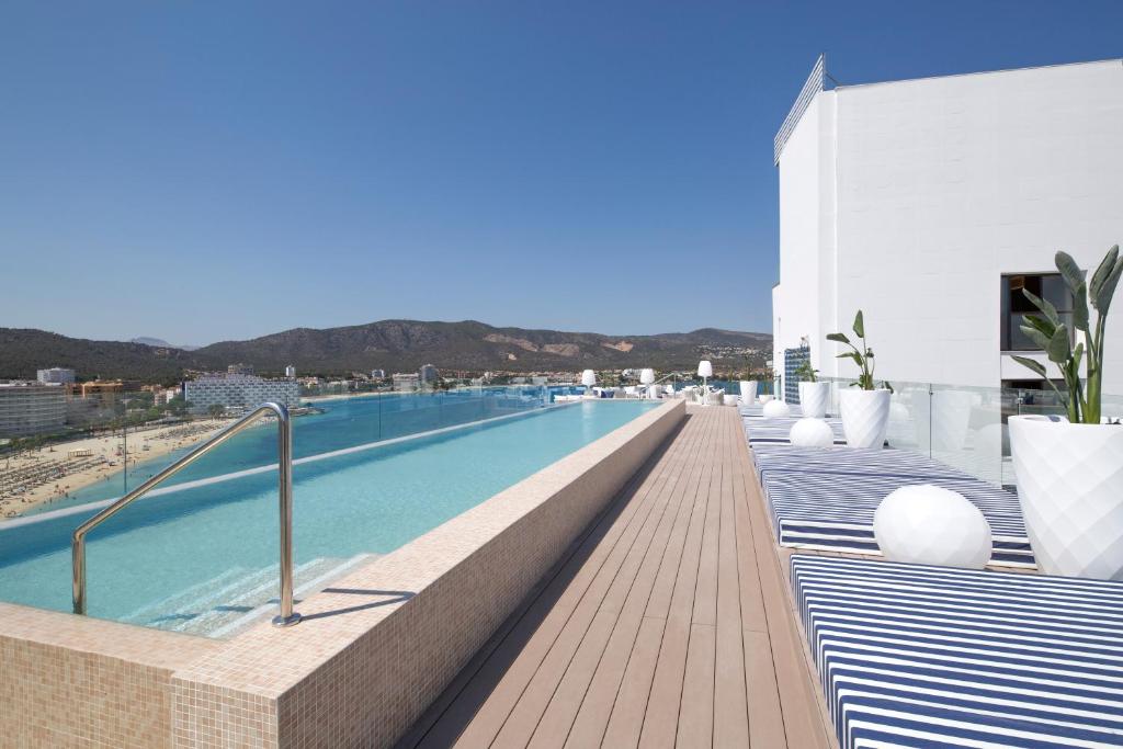 Mūsdienīgs jumta baseins ar skatu uz kalniem un pludmali, apjozts ar stilīgām sauļošanās vietām un zaļiem augiem. Ideāla vieta atpūtai un relaksācijai.