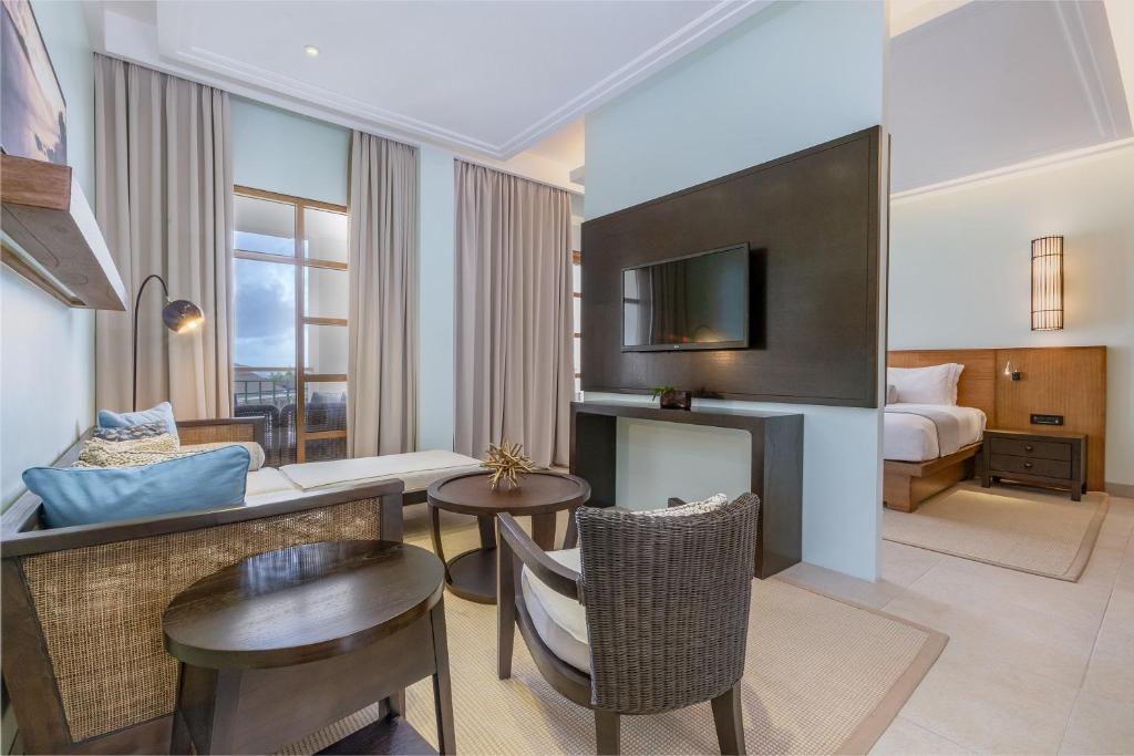 Moderns viesnīcas numurs ar gaišu interjeru, iekārtots ar ērtu dīvānu, galdiņu un televizoru. Liela logs nodrošina dabisko apgaismojumu un skatu uz ārpusi.