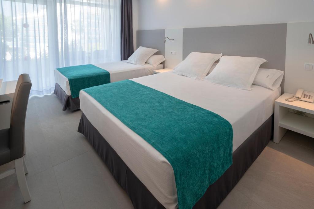 Mūsdienīgs viesnīcas numurs ar divām gultām, kas dekorētas ar gaišu segas audumu un zilzaļiem palagiem, kas piešķir telpai svaigumu. Lielas logu malas ļauj ieplūst dabiskajai gaismai.