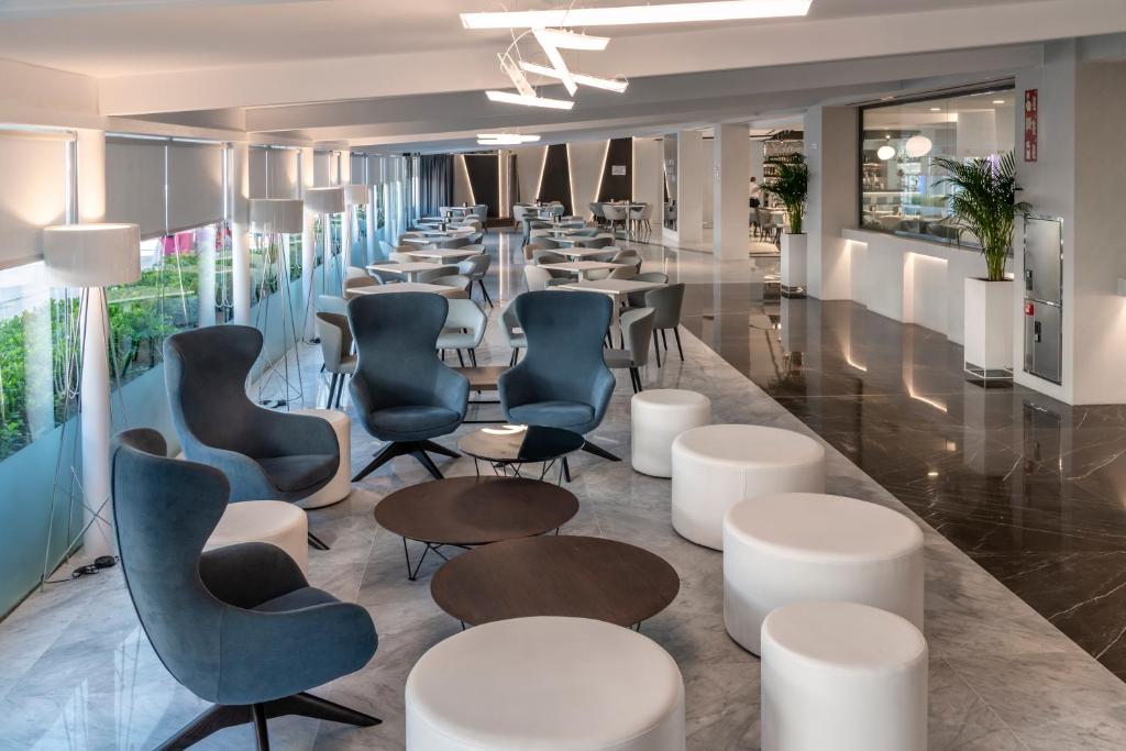 Mūsdienīgs un elegants interjers ar stilīgām atpūtas zonām, kas iekļauj komfortablas krēslus un apaļus galdiņus, radot patīkamu atmosfēru. Gaismas un telpas plānojums veicina relaksāciju un sociālo mijiedarbību.