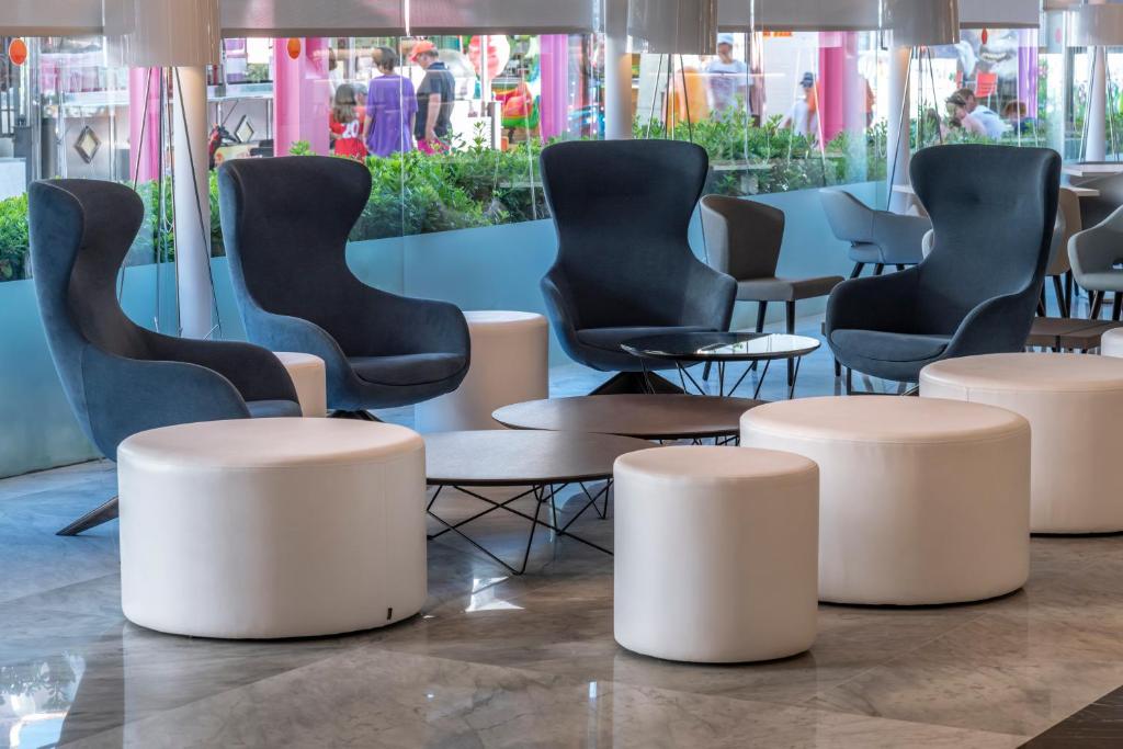 Mūsdienīgs interjers ar stilīgām pelēkām krēslam un baltām apaļām tabulām, radot relaksējošu atmosfēru. Logi ļauj redzēt dārza ainavu ārpusē.