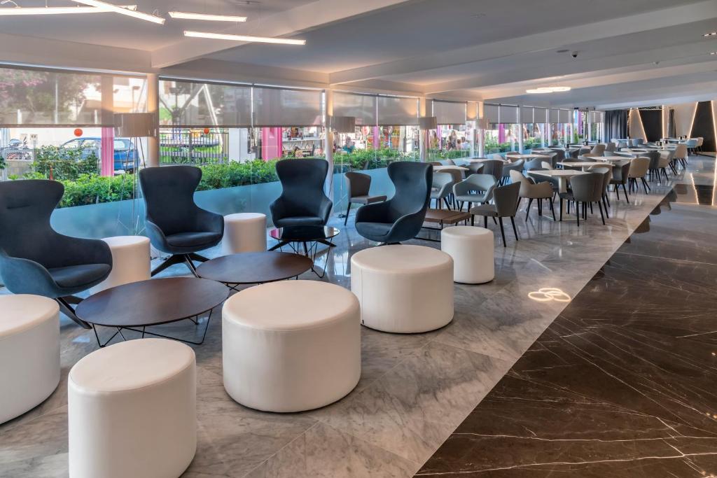 Mūsdienīgs kafejnīcas interjers ar stilīgām atpūtas krēsliem un apaļiem galdiem, kas rada patīkamu atmosfēru. Labi apgaismots ar logiem, kas nodrošina skatu uz ārpusi.