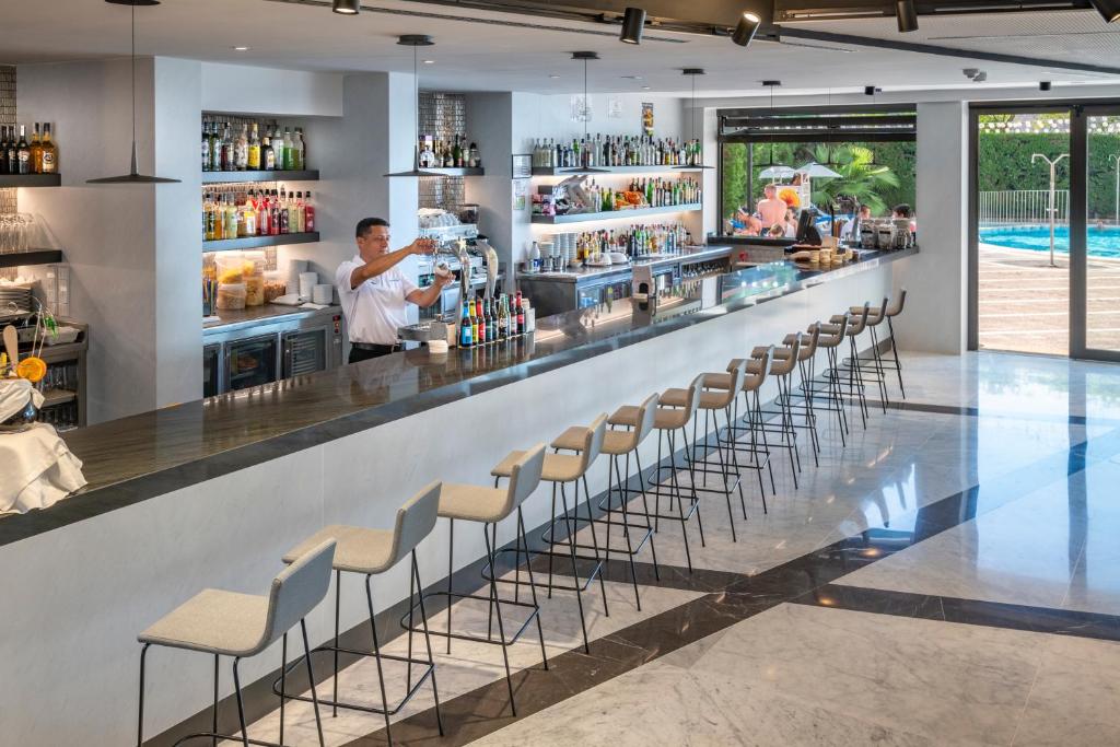 Mūsdienīgs bārs ar garu letes zonu, kur bārmenis gatavo dzērienus, fons ar plašu alkoholisko dzērienu sortimentu. Aiz letes redzama peldbaseina zona un ērtas krēslu rindas.