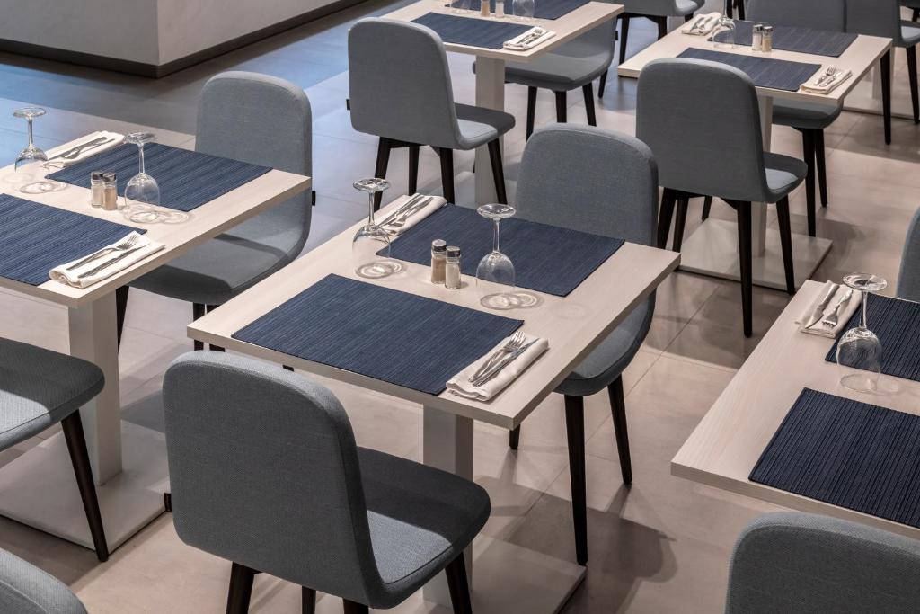 Mūsdienīgs restorāna interjers ar elegantām galdiem, zilu galda piederumu un krēslu komplektu, radot viesmīlīgu atmosfēru.