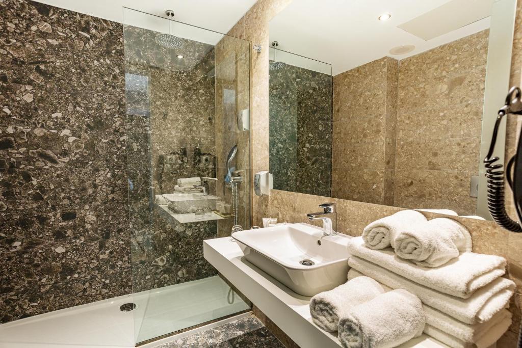 Mūsdienīga vannas istaba ar akmens apdari, stikla dušas kabīni un tīrām dvieļiem. Elegants dizains, kas nodrošina komfortu un stilu.