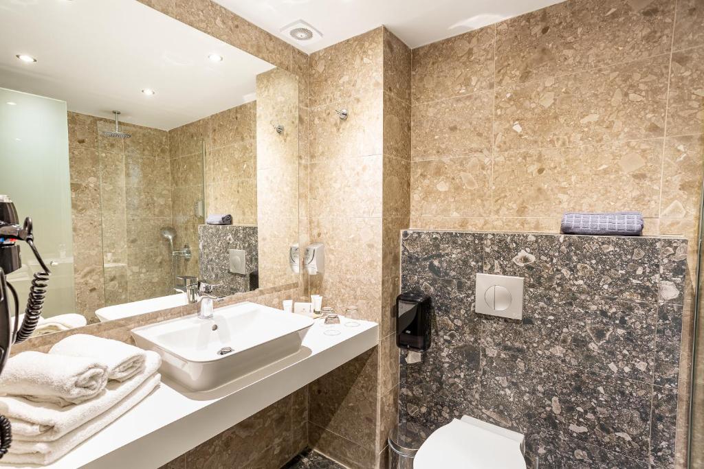 Mūsdienīgs vannas istabas interjers ar akmens apdari, gaišām flīzēm un elegantu izlietni. Telpā ir arī vannas piederumi un dvieļi, radot patīkamu atmosfēru.