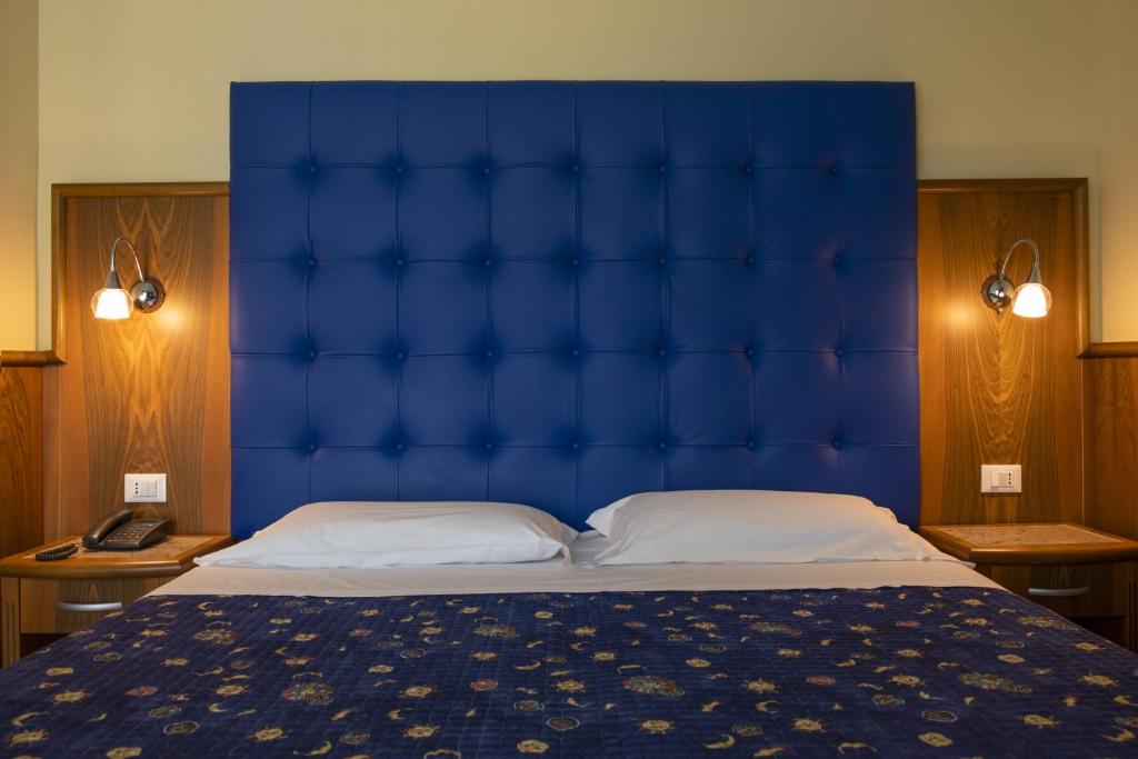 Mūsdienīga guļamistaba ar zilu, izšūtu gultas galvu un naktslampām abās pusēs, radot komfortablu un stilīgu atmosfēru.