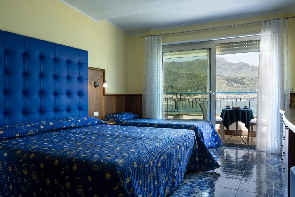 Mūsdienīgs viesnīcas numurs ar divām gultām un zilu interjeru, kas piedāvā skaistu skatu uz kalniem un jūru. Numurā ir balkons, kurā ir galdiņš un krēsli.