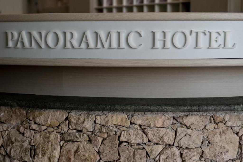 Reģistratūras galds ar izteiksmīgu "PANORAMIC HOTEL" uzrakstu, kas izveidots no koka un akmens materiāliem. Šis dizains rada viesmīlīgu un modernu atmosfēru.
