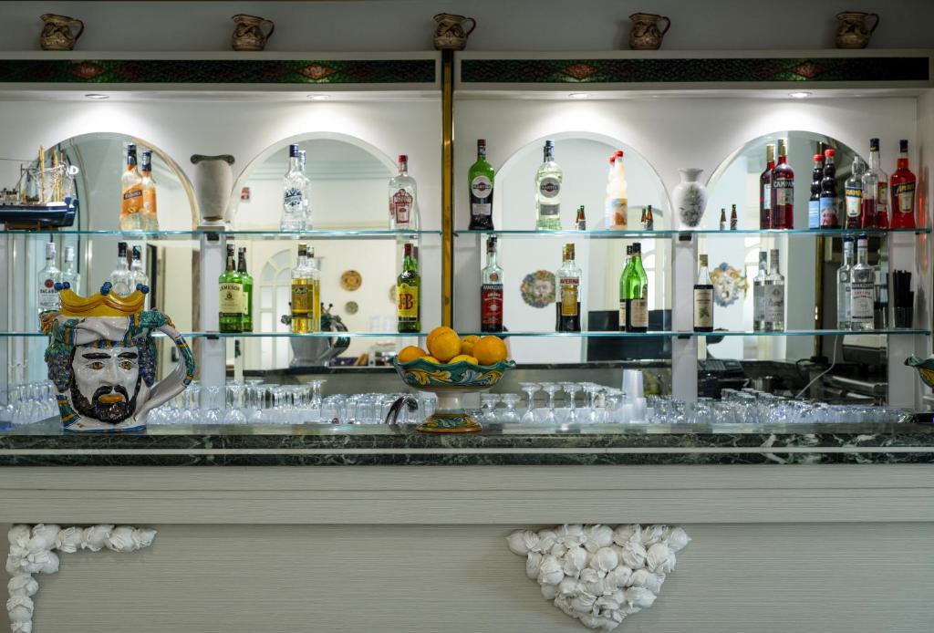 Bārs ar elegantu interjeru, kurā redzama plaša dzērienu izvēle un dekoratīvs trauks ar apelsīniem. Uz letes ir krāšņs māla trauks ar seju, kas piešķir unikālu raksturu.