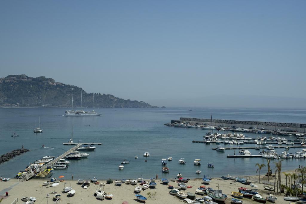 Jūras kreisā krasta ainava ar kuģiem un laivām ostā, kalnu fons un skaidrs debesis. Pludmale ar smiltīm un dažādām laivām, kas izkaisītas krastā.