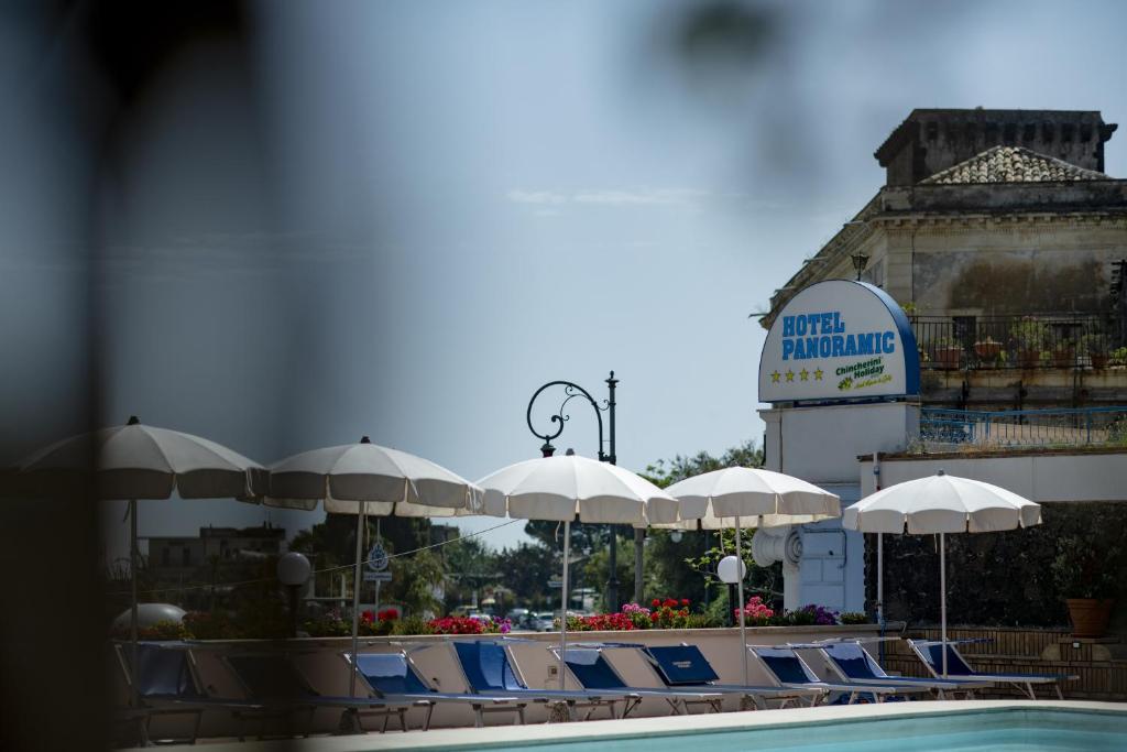 Vasaras kūrorts ar peldbaseinu un saulessargiem, fons ir viesnīcas "Hotel Panoramic" zīme.