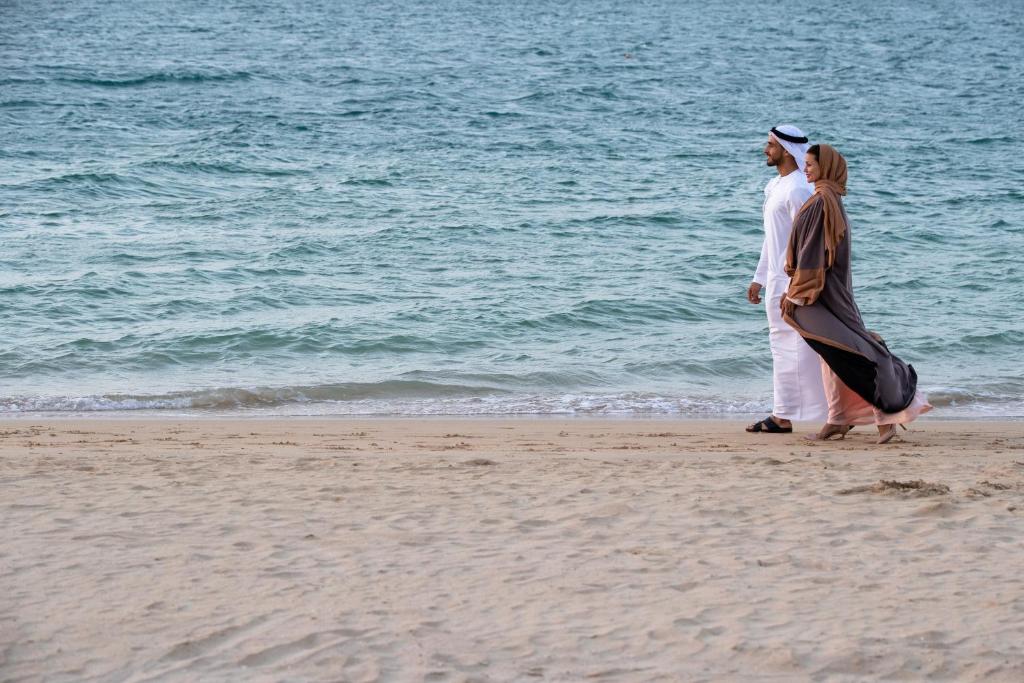 Pāris staigā gar pludmali, baudot jūras skaņas un mierīgu atmosfēru. Viņi ir ģērbušies tradicionālās apģērbos, izceļot kultūras bagātību.