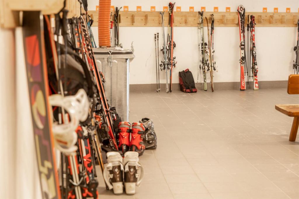 Sniega sporta inventāra telpa ar slēpēm, slēpju apaviem un citiem piederumiem, kas sakārtoti pie sienas un uz grīdas. Ideāla vieta, lai sagatavotos ziemas priekam.