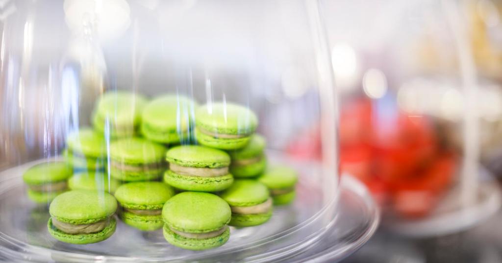 Zaļie makaroni uz pasniegšanas trauka, ar gaišu fonu un izplūdušām krāsām. Šis attēls izceļ gardēžu deserts, kas ir populārs konditorejā.