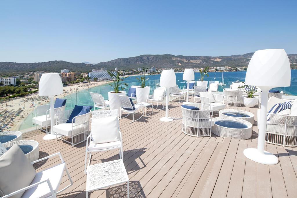 Moderns jumta bārs ar baltām mēbelēm, skats uz pludmali un jūru, saulains laiks un kalnu ainava fona.