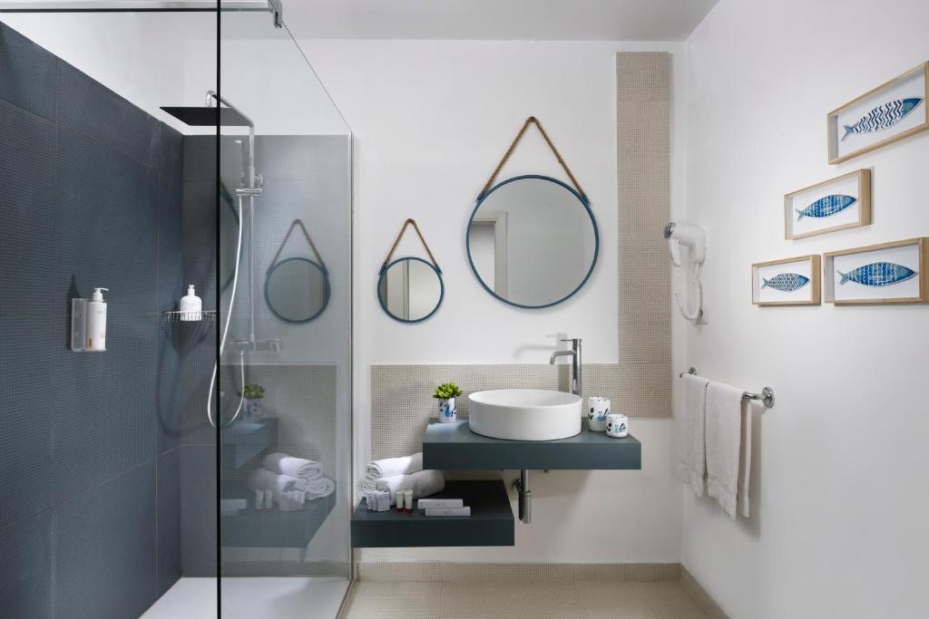 Mūsdienīga vannas istaba ar stikla dušu, apaļu spoguli un stilīgu izlietni. Interjerā ir izmantoti pelēki toņi un jūras motīvi, radot svaigu un relaksējošu atmosfēru.