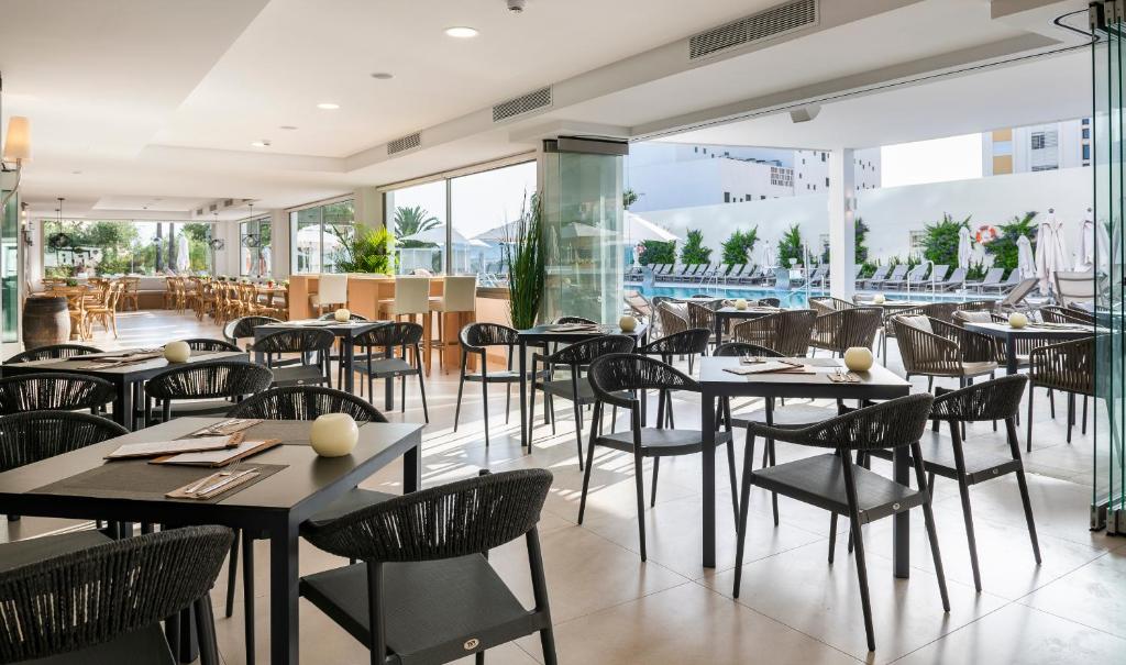 Mūsdienīgs restorāns ar plašiem logiem, kas piedāvā skatu uz peldbaseinu. Melni galdi un krēsli rada elegantu atmosfēru.