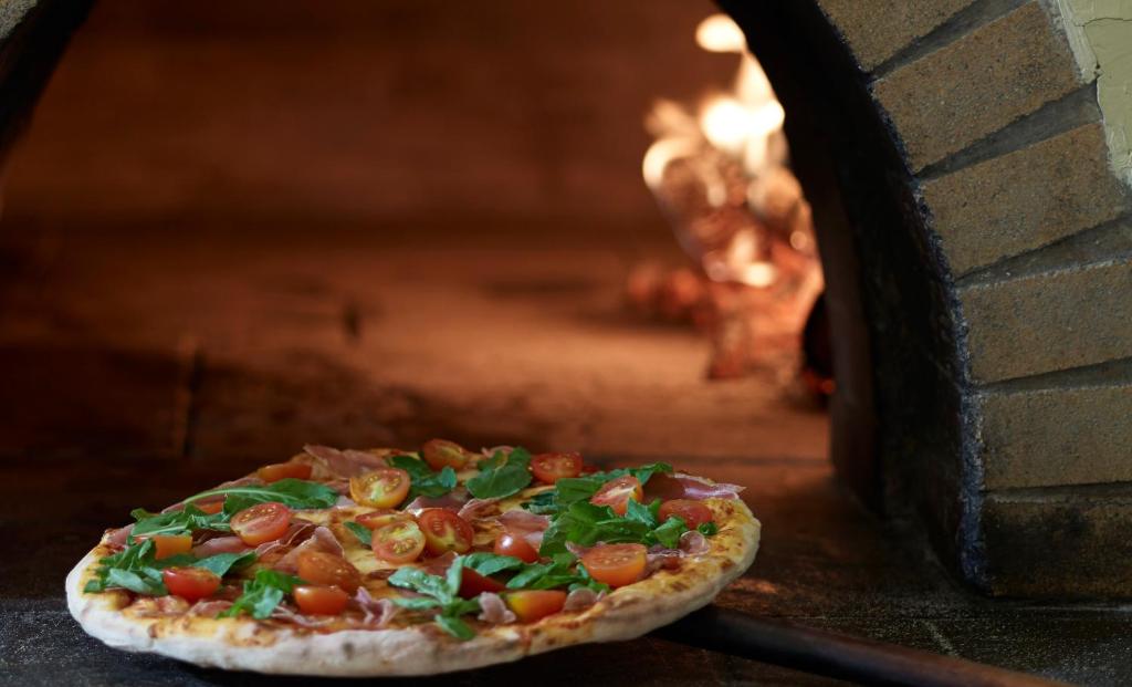 Pica ar tomātiem, rukolu un šķiņķi, kas cepta koka krāsnī, radot sulīgu un garšīgu ēdienu.