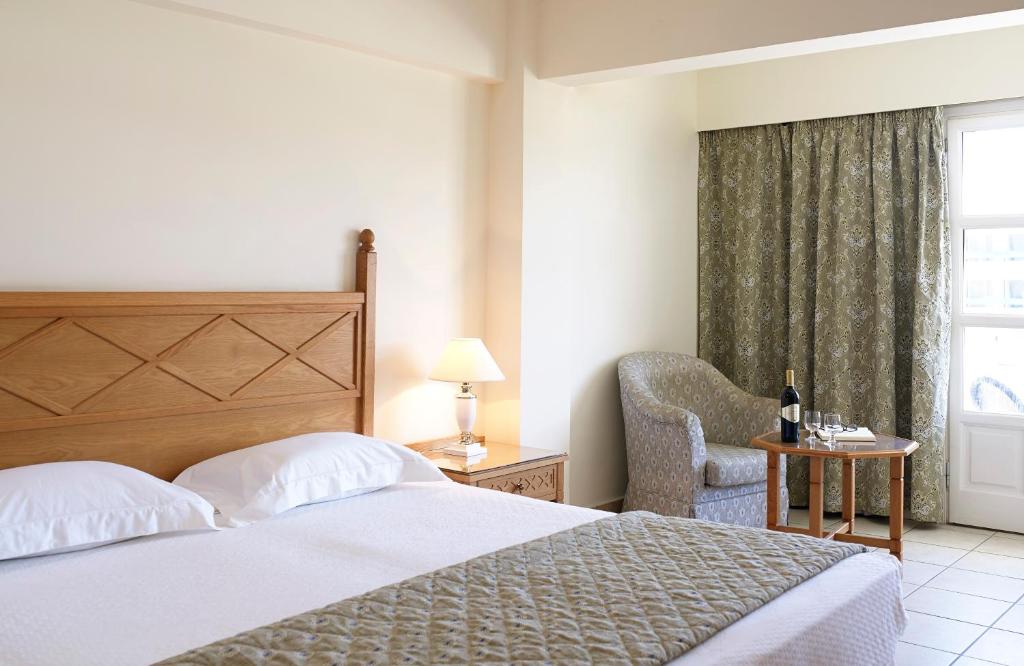 Mūsdienīgs viesnīcas numurs ar divguļamo gultu, ērtu atpūtas krēslu un galdiņu, kas dekorēts ar vīna pudeli un glāzēm. Logā redzami aizkaru audumi un dabīgā apgaismojuma efekti.