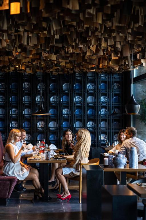 Elegants restorāns ar stilīgu interjeru, kur grupiņa cilvēku baudīja vakariņas un sarunas. Gaismas spēles un mūsdienīgs dizains rada patīkamu atmosfēru.