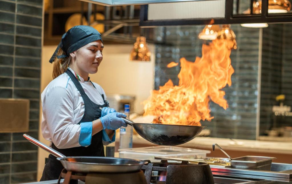 Šefpavārs, kas strādā virtuvē ar uguni un izsist krāsota pannu, radot dramatisku gaisotni.