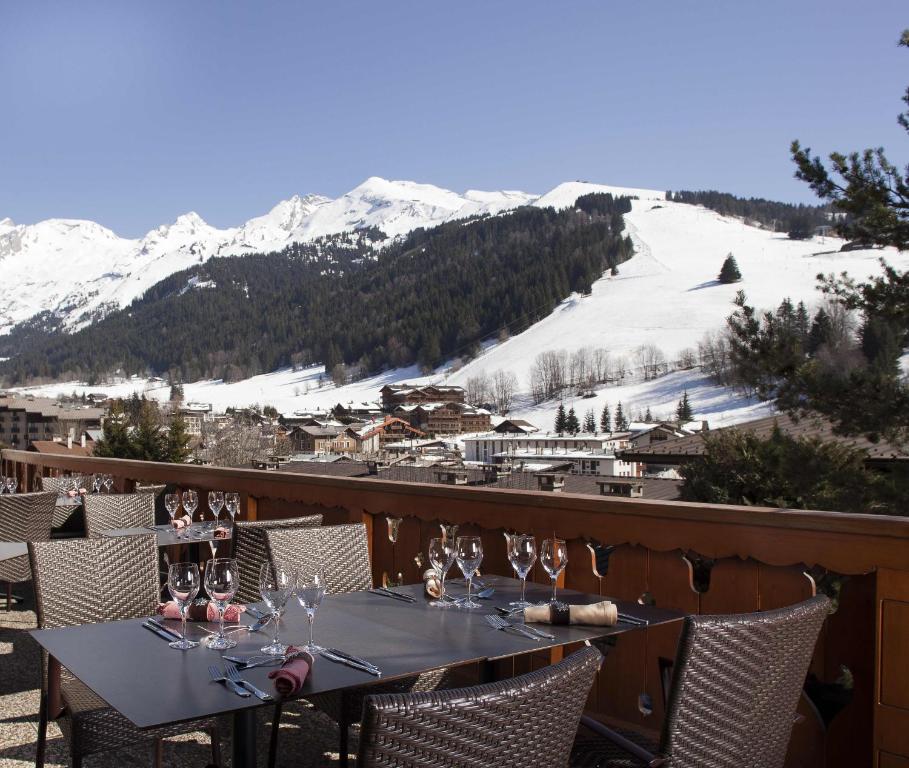 Terases galdi ar glāzēm un piederumiem, kas atrodas ar kalnu ainavu fona. Apkārt sniegoti pakalni un meži, radot mierīgu atmosfēru.