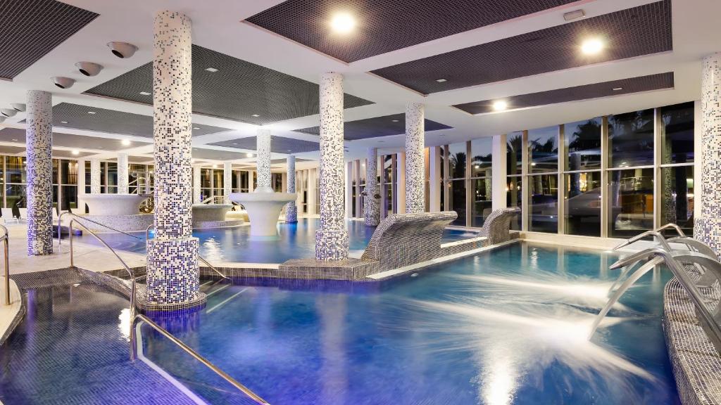 Mūsdienīgs spa centrs ar lielu iekšējo baseinu, masāžas strūklakām un elegantiem mozaīkas elementiem. Gaisma un plašums rada relaksējošu atmosfēru.